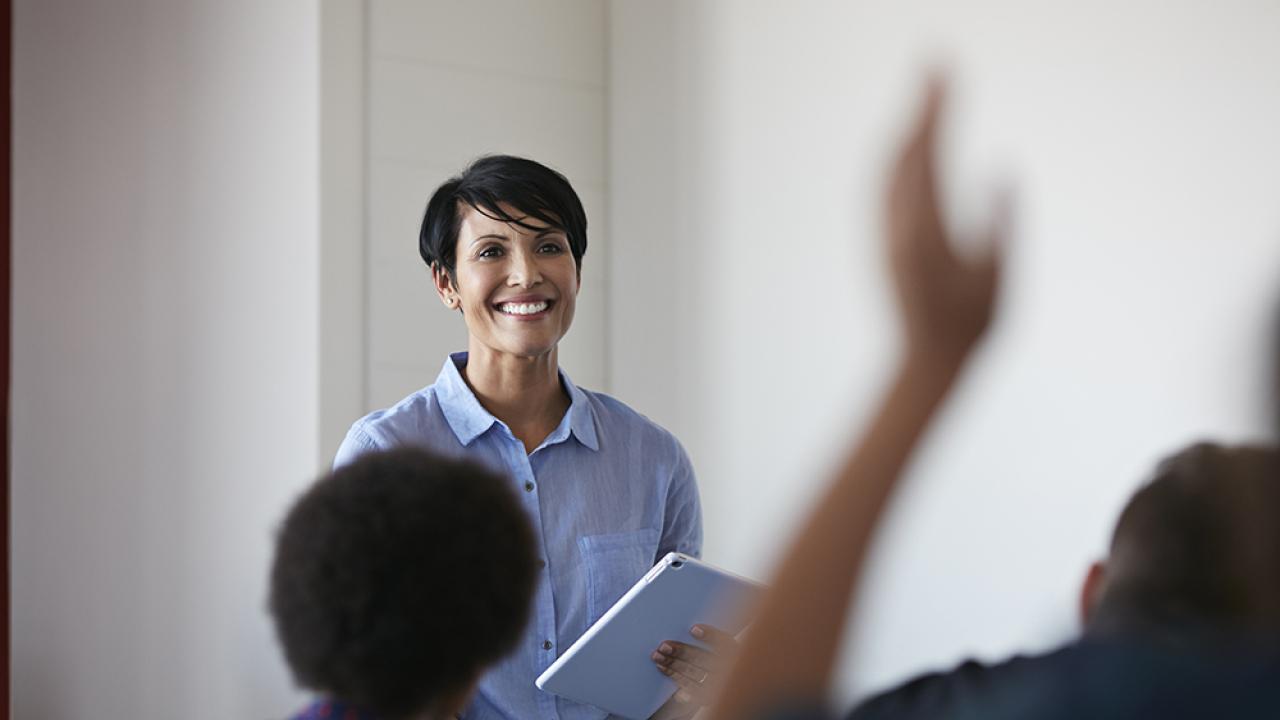 teacher in front of classroom with a student hand raised
