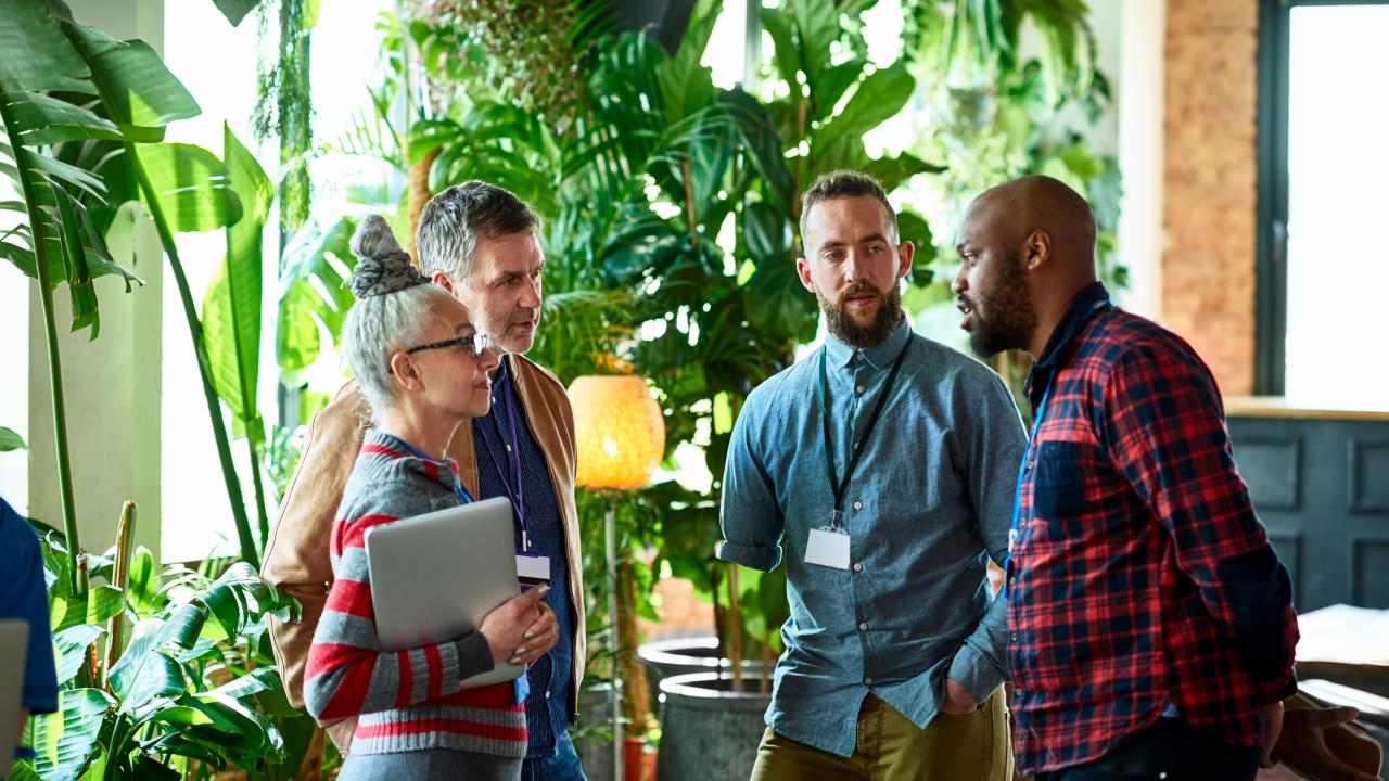 Four colleagues speak to each other in an office setting.