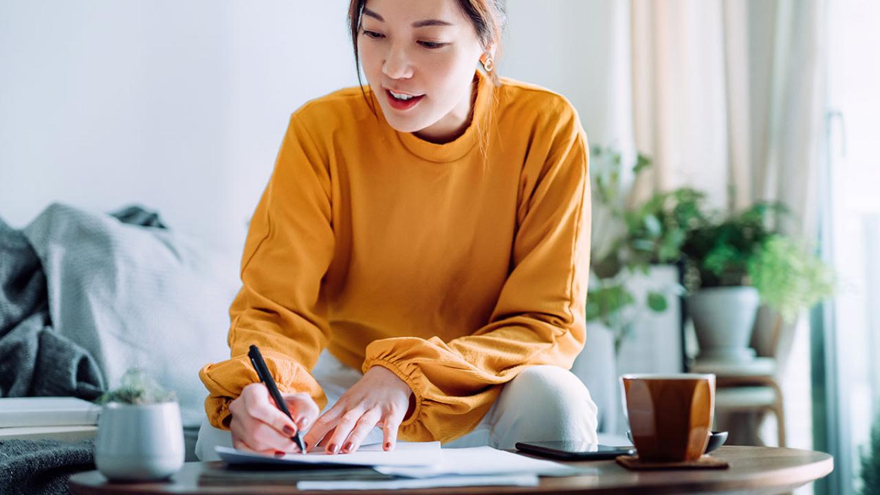 a woman holding a pen and signing paperwork in the living room at home