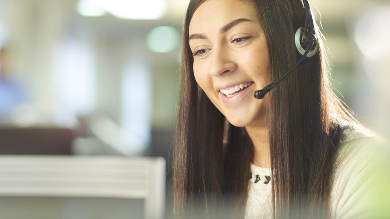 a woman with a phone headset on smiles while talking 