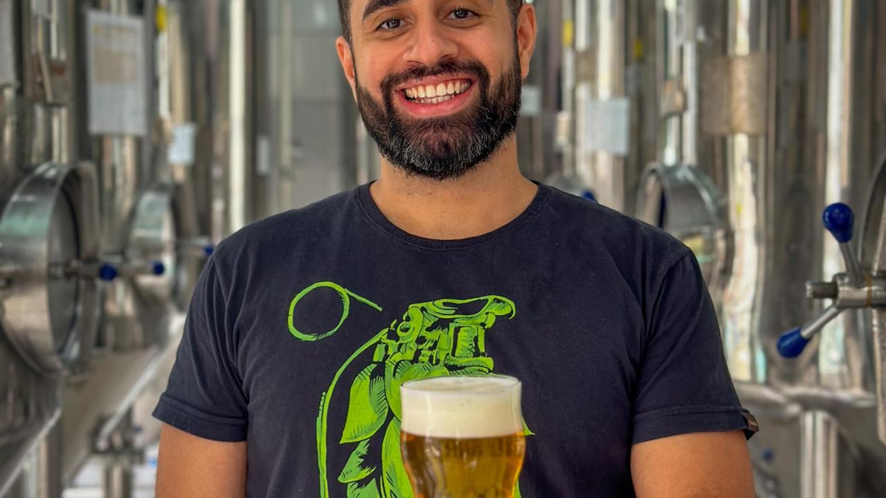 Michael and Sheila Lewis Brewing Scholarship winner Matheus Ramos poses with a glass of beer in a brewery