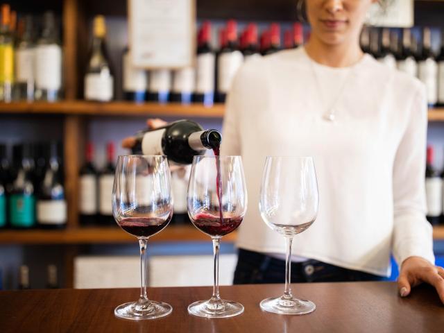 Woman in tasting room pouring red wine into three glasses