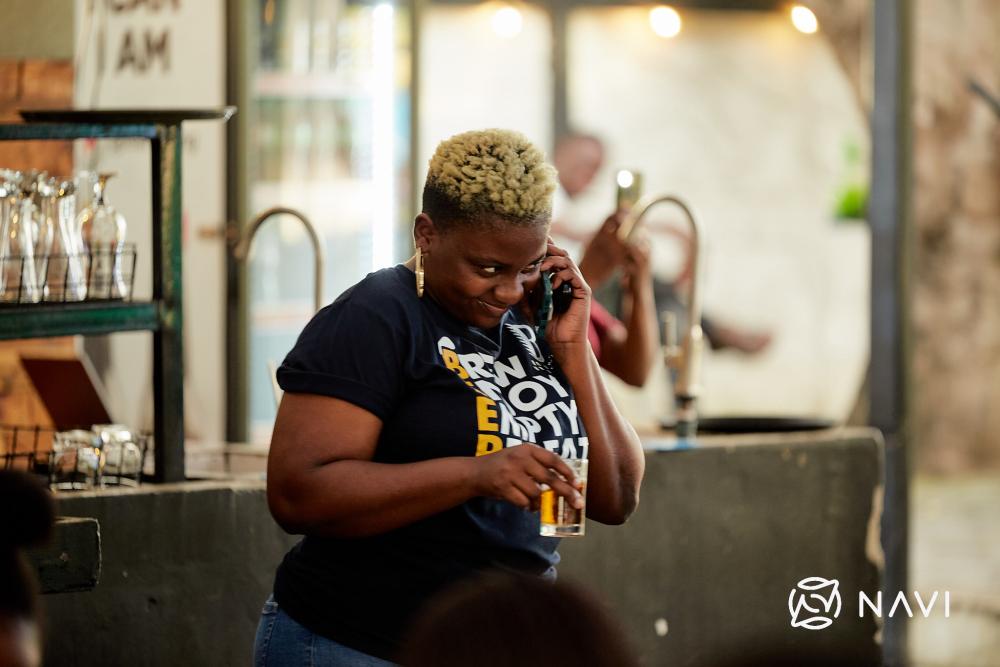 Chijindu Onwuchekwa in brewery holding a beer and smiling while on the phone