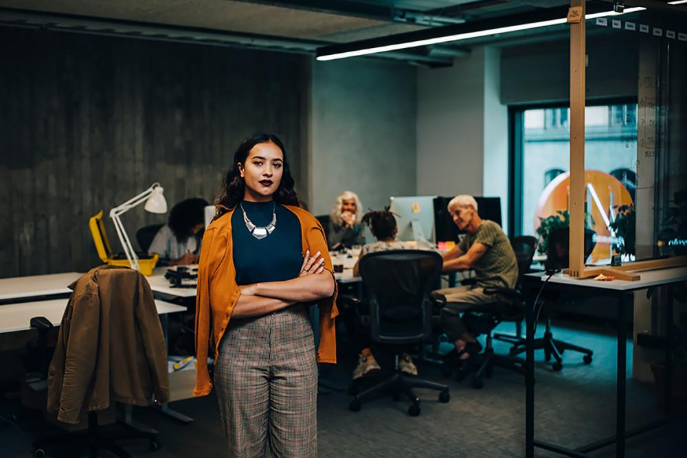woman standing in foreground of conference room as colleagues meet behind her