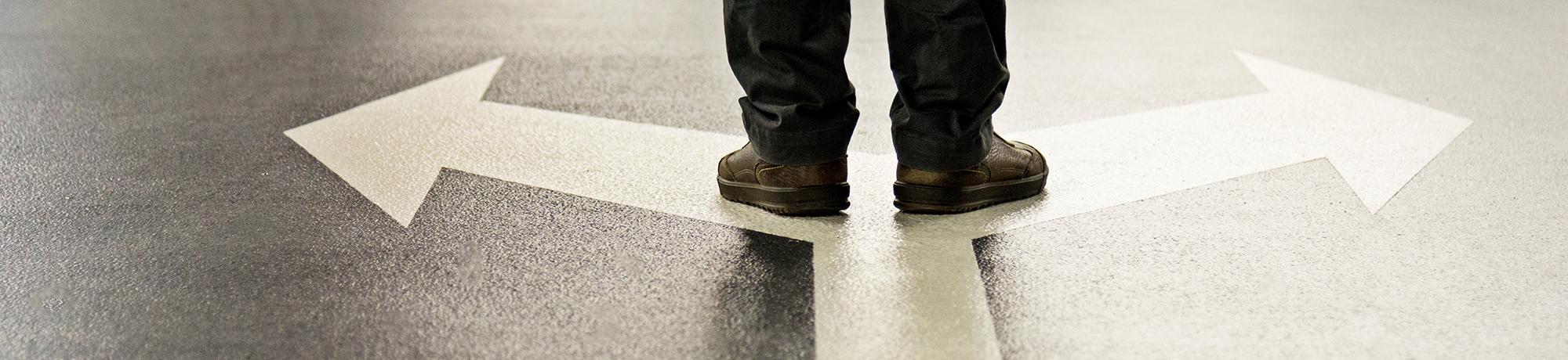 man standing on arrows pointing in opposite directions painted on a floor